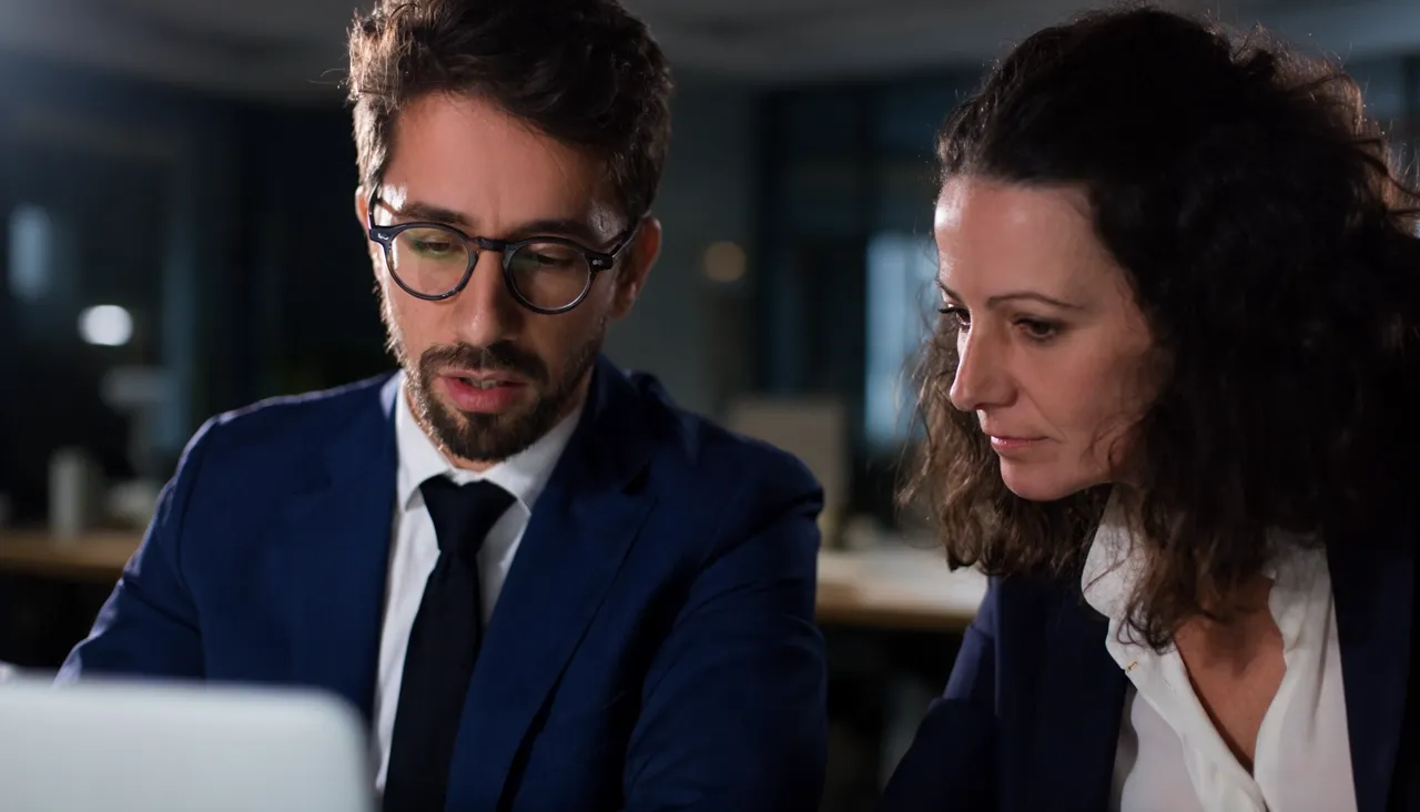 Two business professionals reviewing information on a laptop in an office