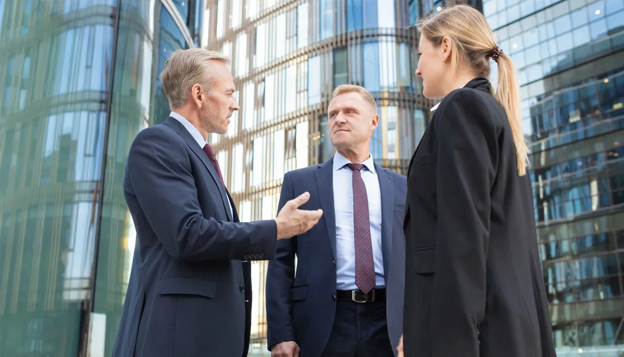 Three business professionals having a discussion outside a modern glass office building