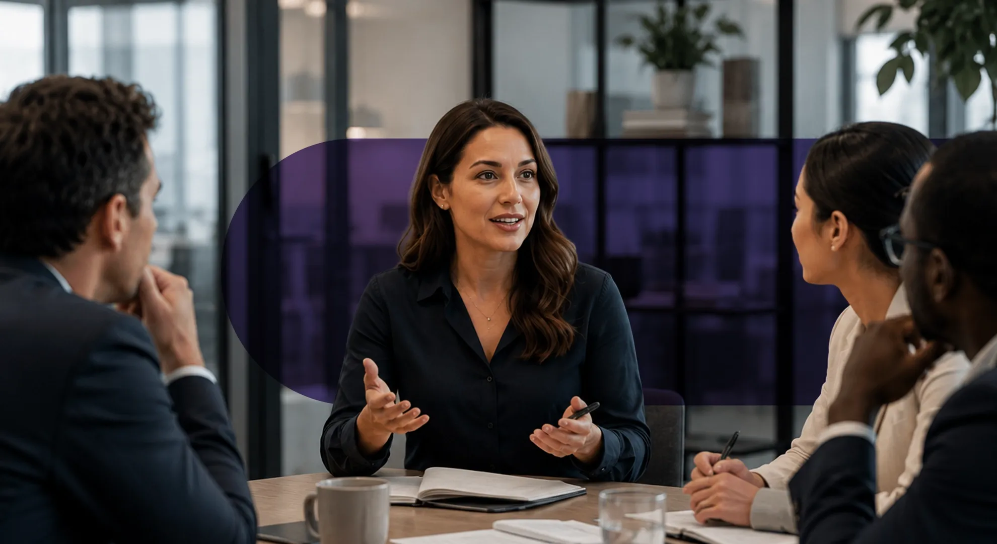 A professional woman speaks and gestures with hands during a business meeting with diverse colleagues.