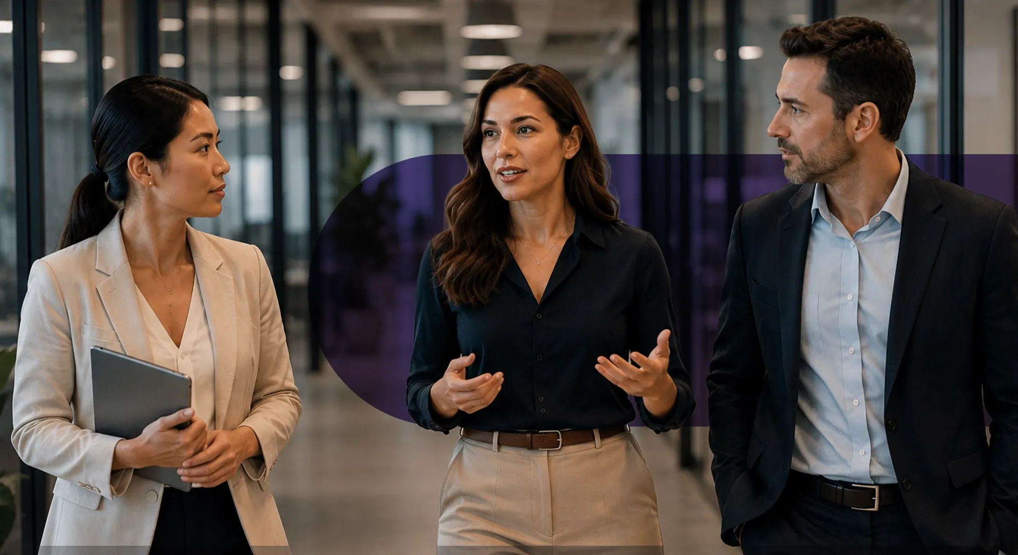 Three diverse business professionals discuss a project while walking through a modern office corridor.