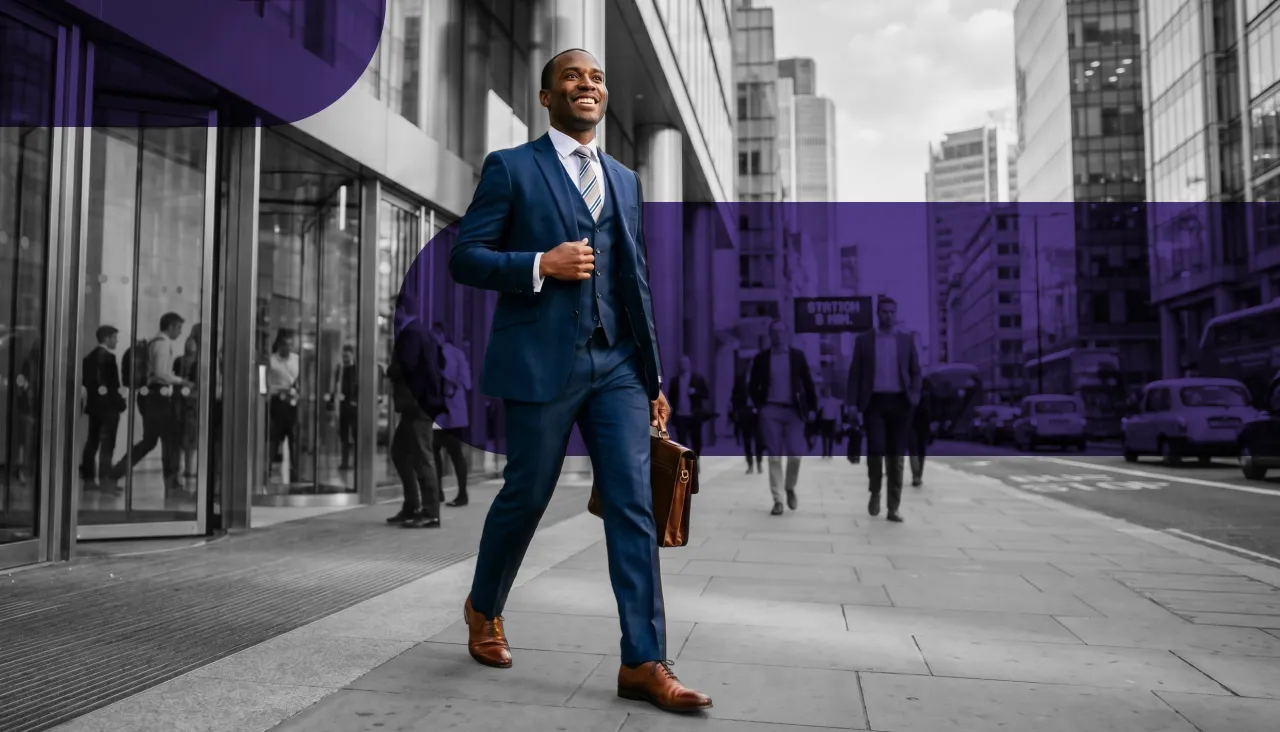 Smiling man in a blue suit walks confidently with a briefcase through a city street.
