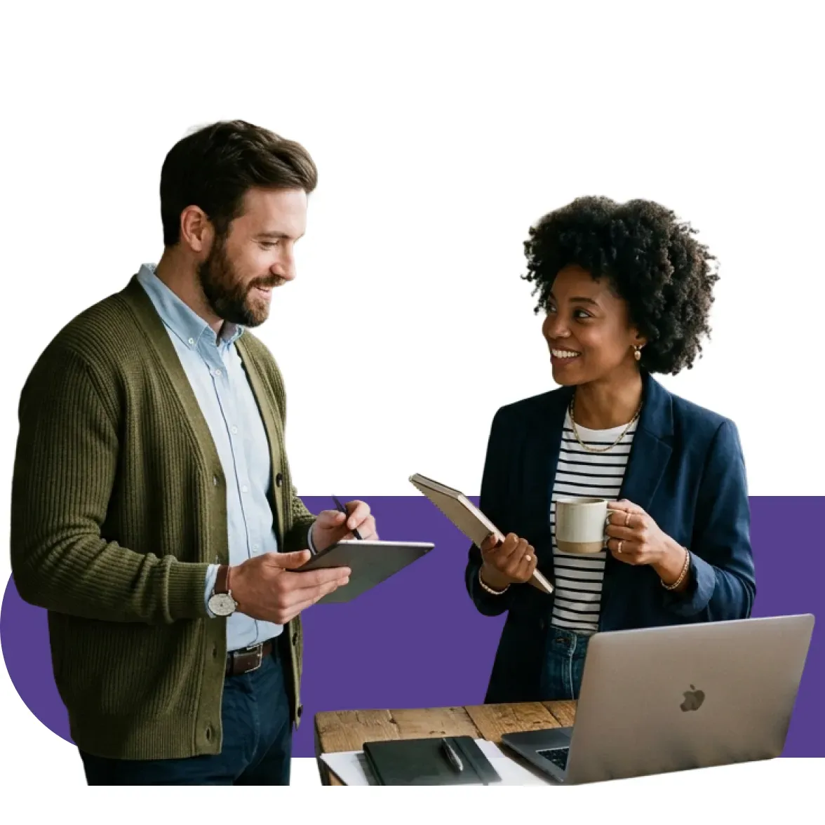 Two diverse colleagues collaboratively discuss work, both smiling and holding tablets.