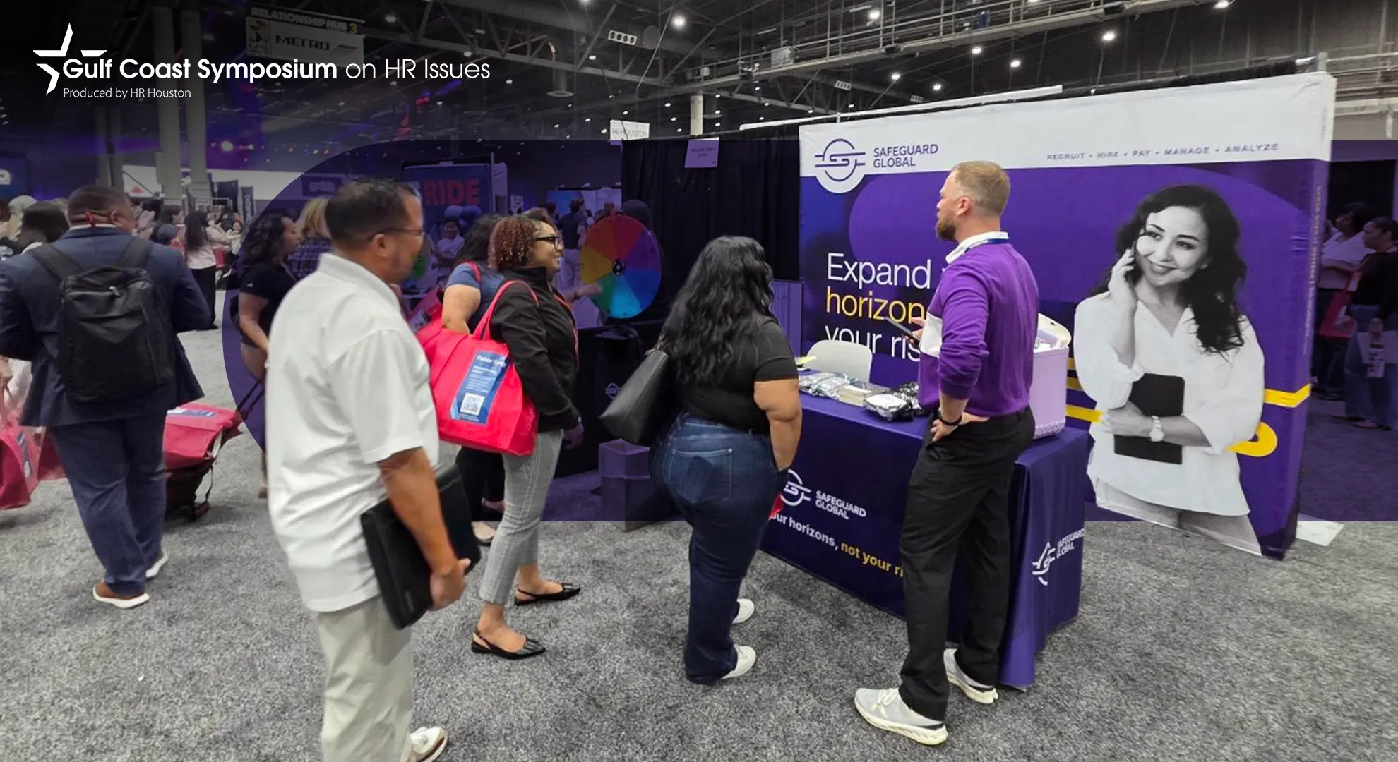 Attendees gather around a purple and white conference booth with a man in a purple shirt.