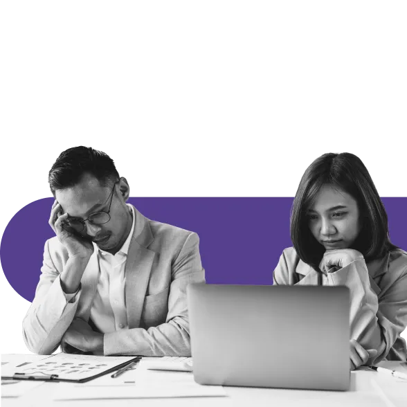Two colleagues look stressed while working at a laptop, one resting their head.