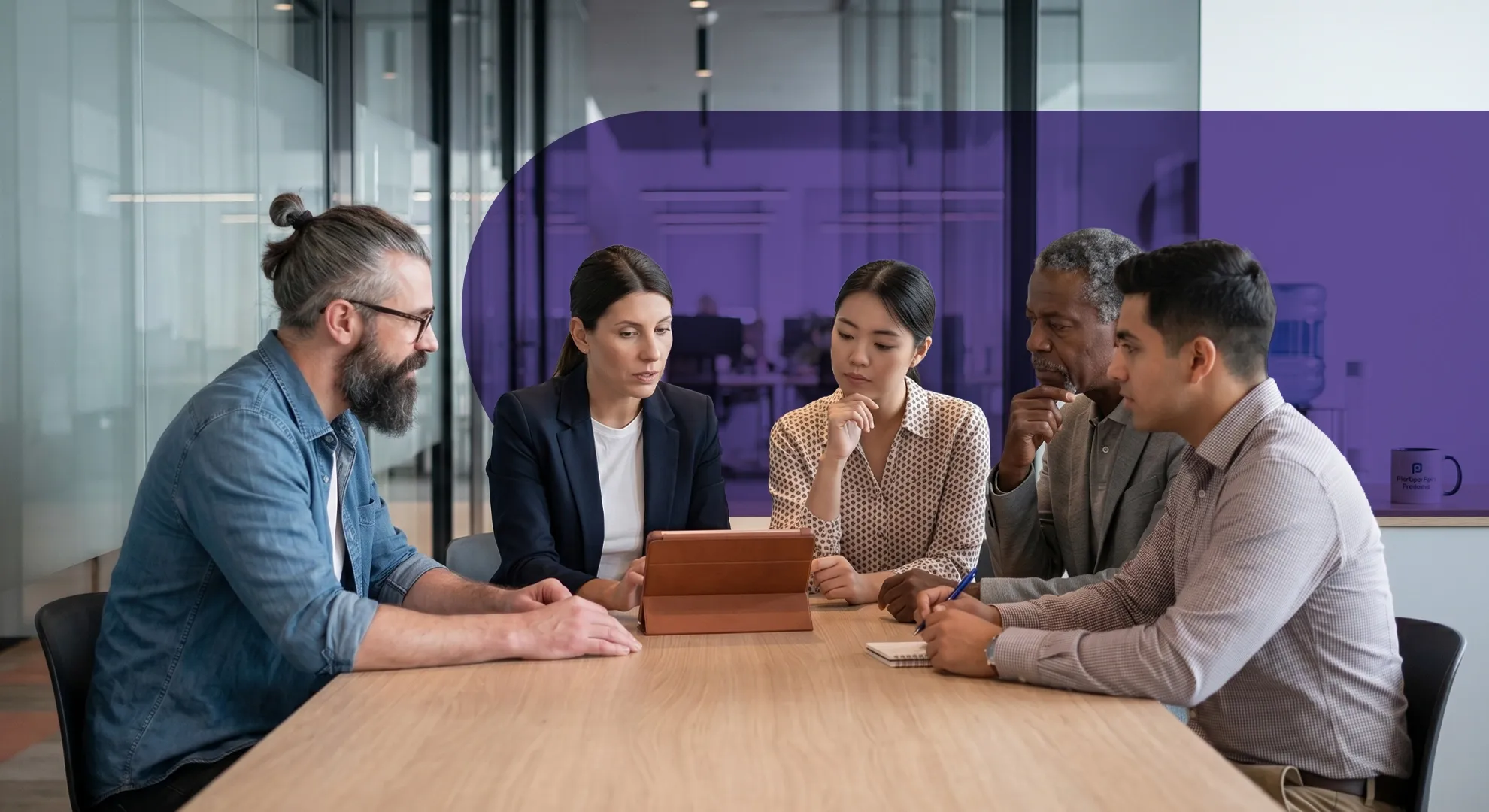 Diverse group of five professionals in a meeting, intently discussing content on a tablet.