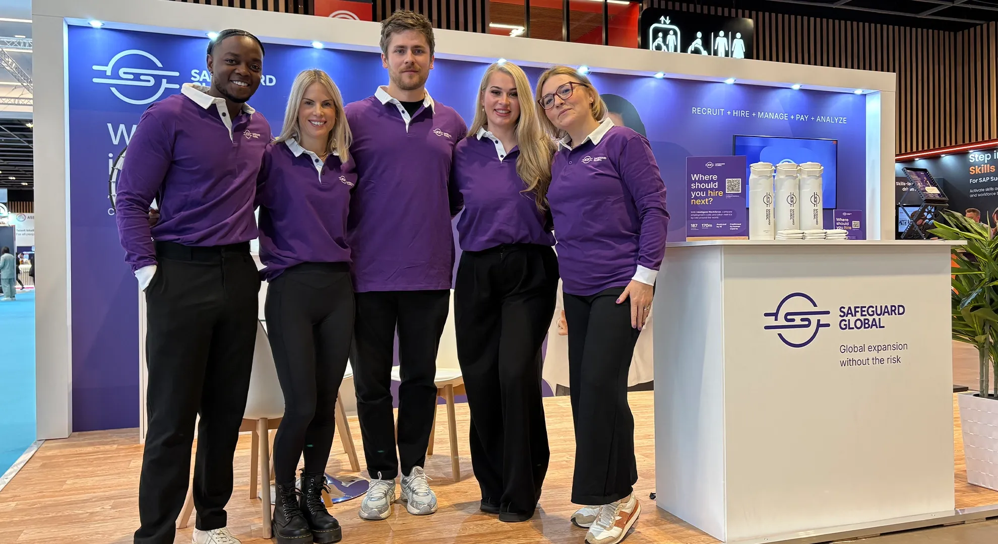Five Safeguard Global team members posing in front of the company's branded exhibition booth at a trade show