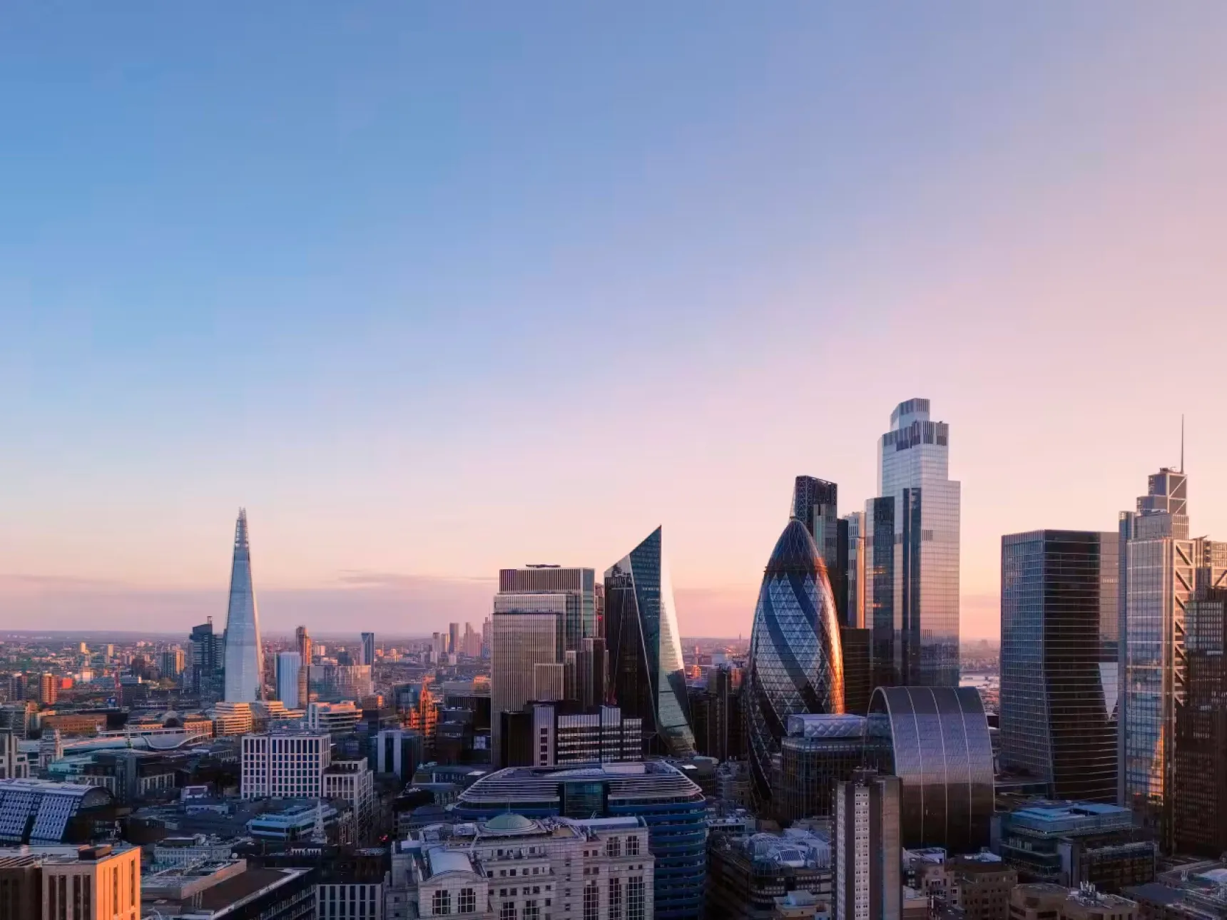 Modern skyscrapers dominate a city skyline against a pastel dawn sky, including The Shard.