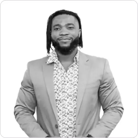 Professional man with dreadlocks and beard in patterned shirt and blazer, smiling subtly.