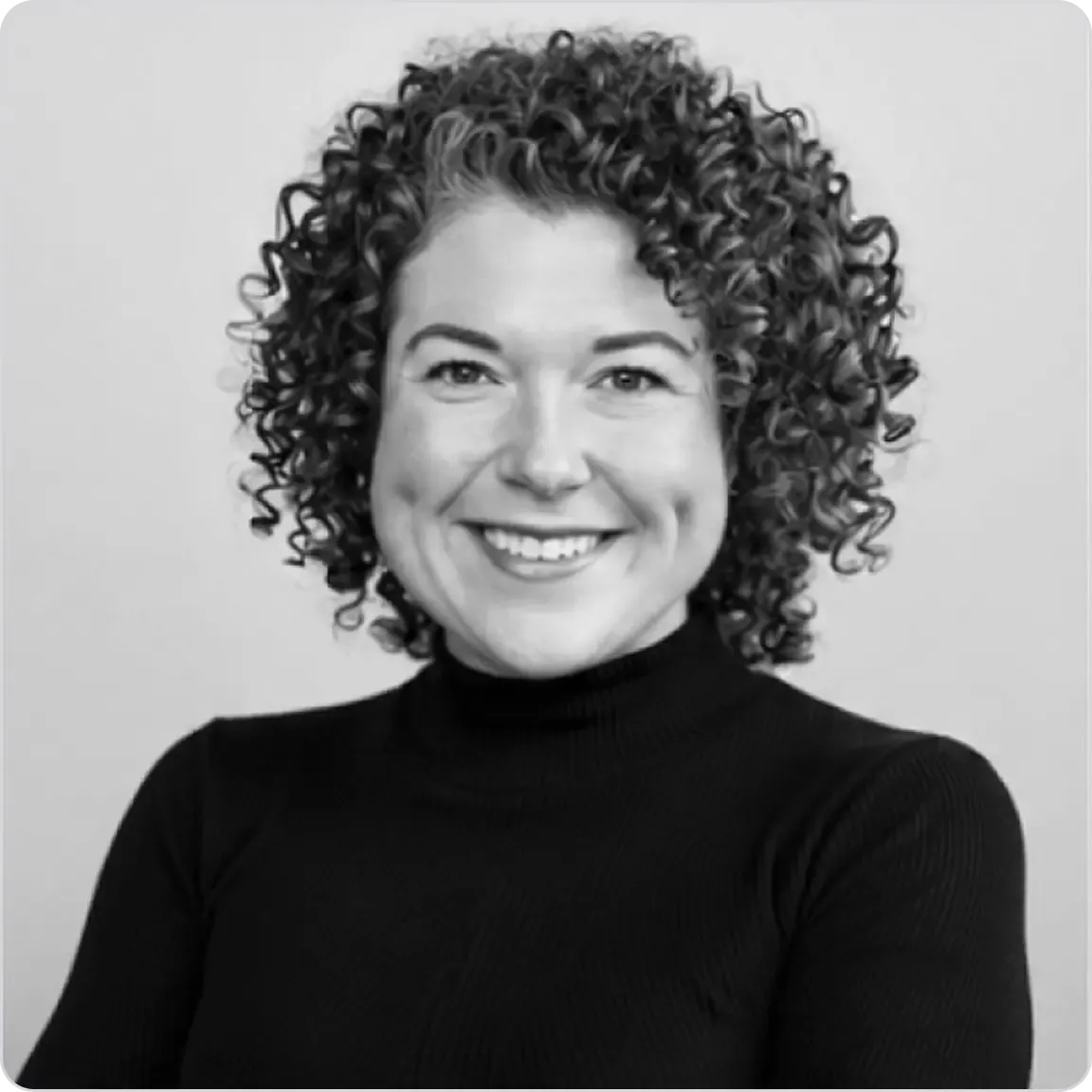 Black and white headshot of a smiling woman with curly hair wearing a dark turtleneck.