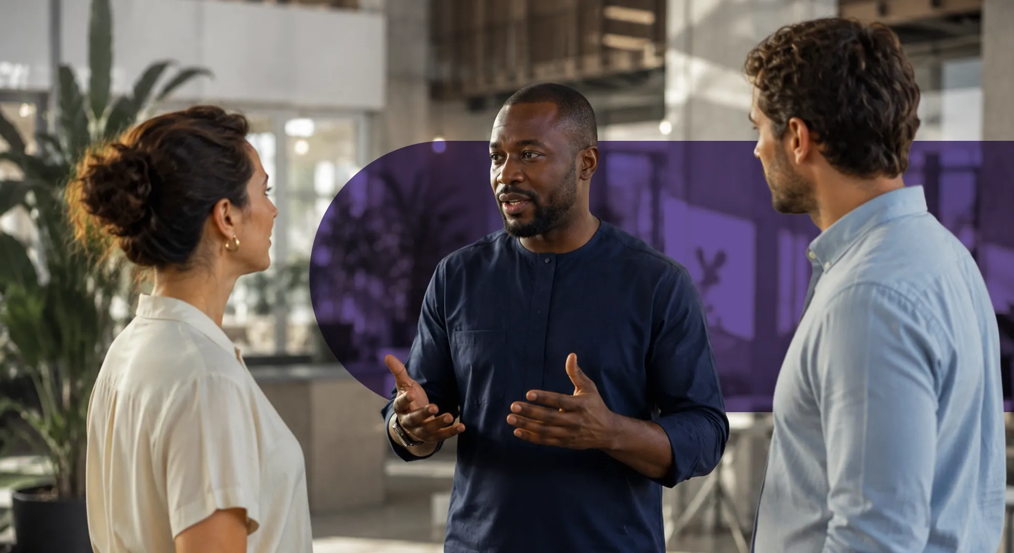 Three diverse professionals discussing in a modern office, man in middle gesturing.