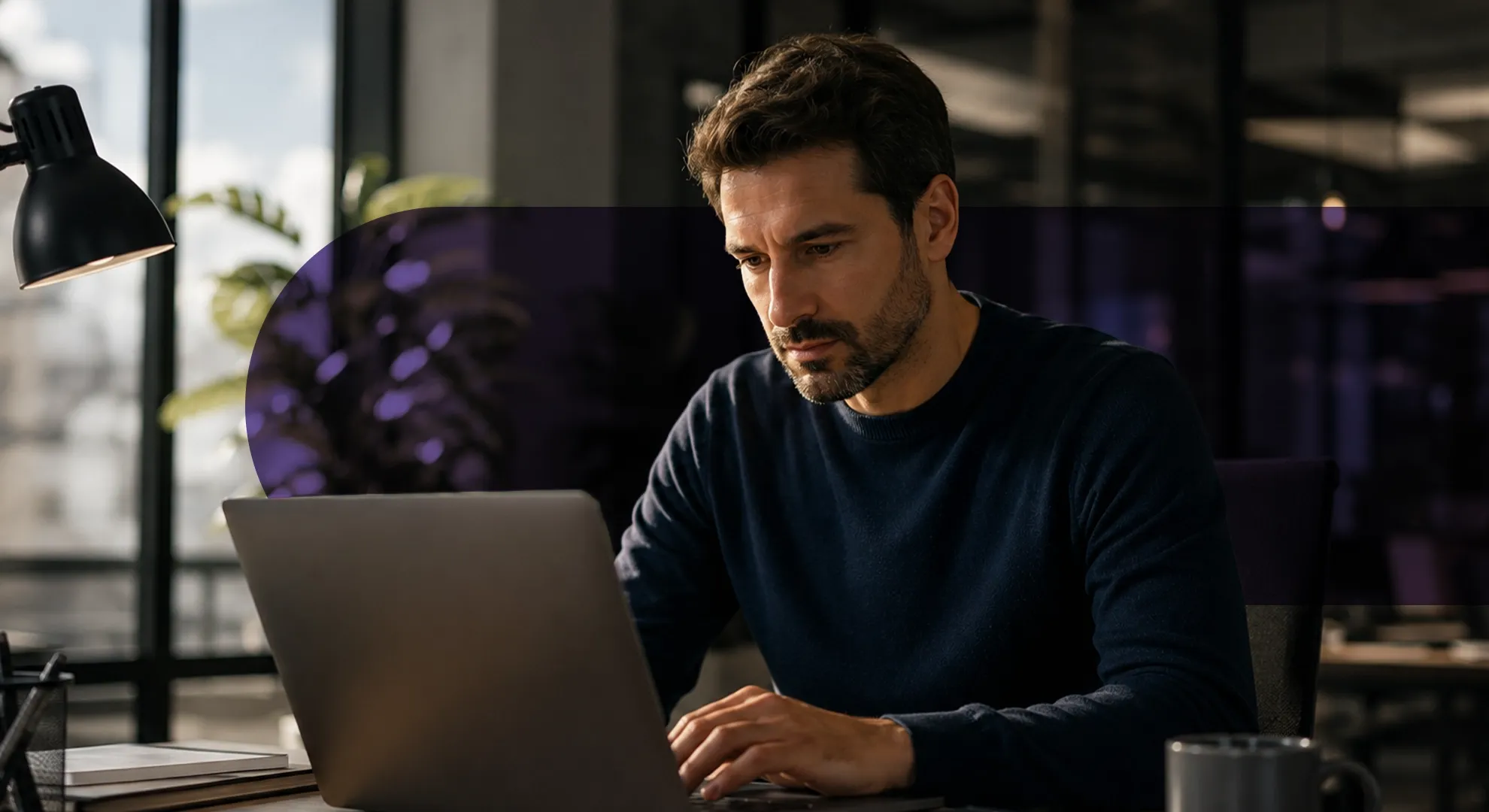 Man working on laptop in a dimly lit office with focused expression.