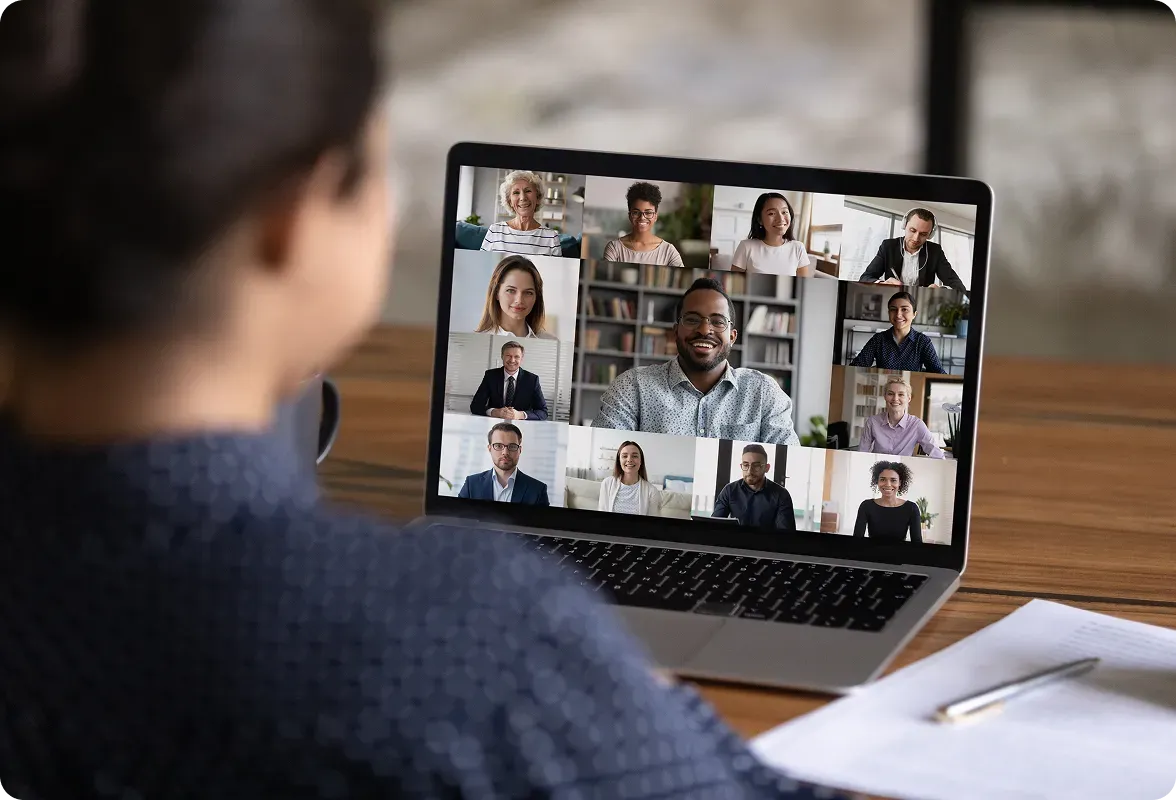 Person views a laptop screen displaying a video conference with diverse participants.