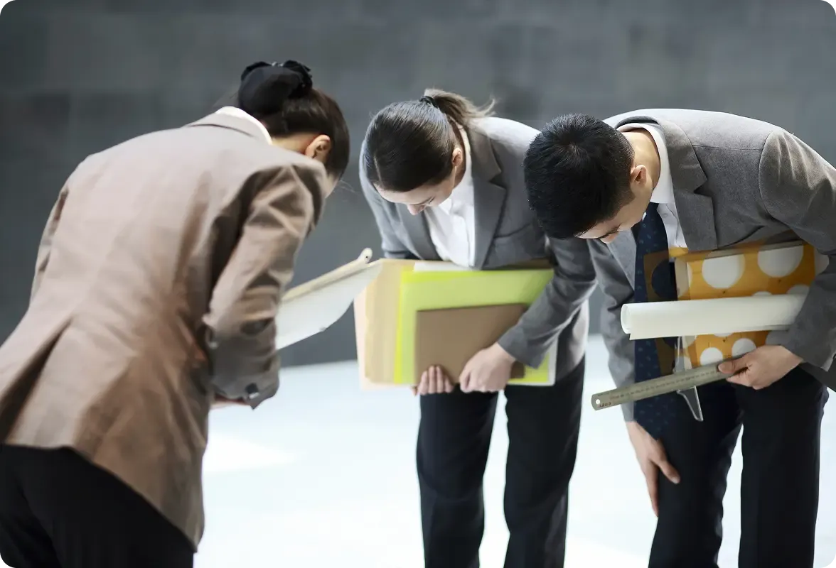 Three business people in suits bending over, intently examining documents and papers on the ground.