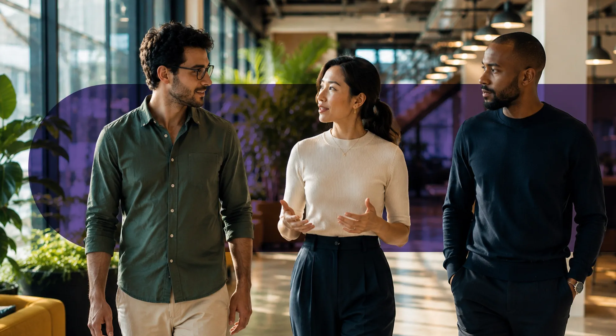 Three diverse professionals walk and converse in a bright, modern office environment.